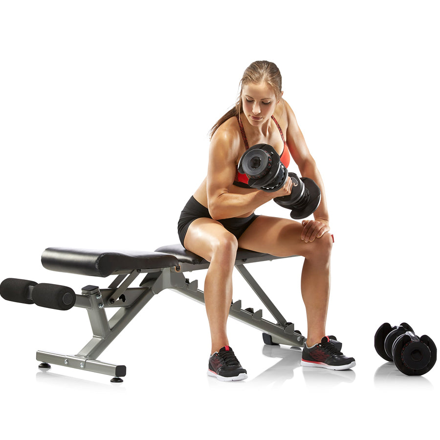 Person seated on a bench with adjustable dumbbells